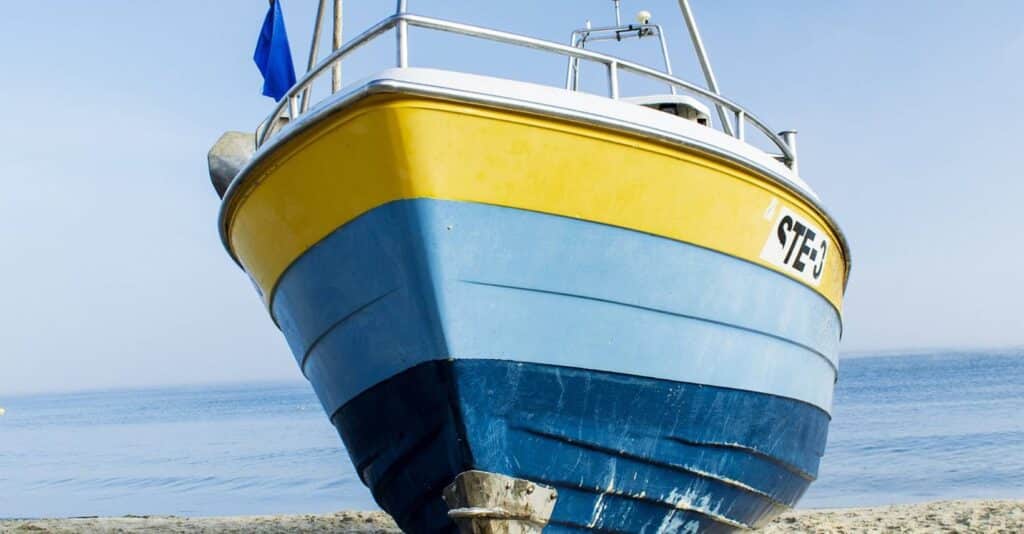 En motorbåt på stranden med ett skrov som är målat i gult, ljusblått och marinblått.