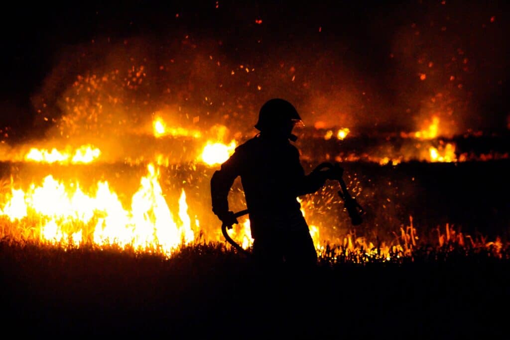 En brandman i svart siluett med en pågående brand i bakgrunden.