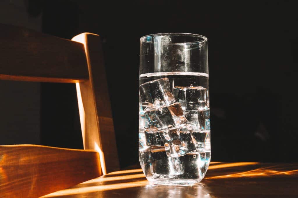 Ett glas vatten på ett träbord mot en mörk bakgrund.