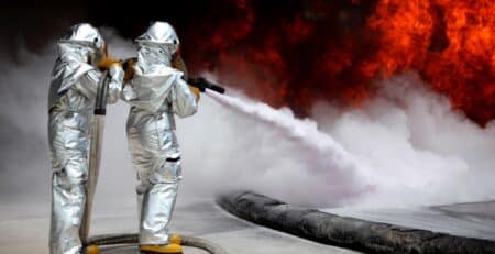 Brandmän i värmeskyddande kläder sprayar släckskum vid en brand.